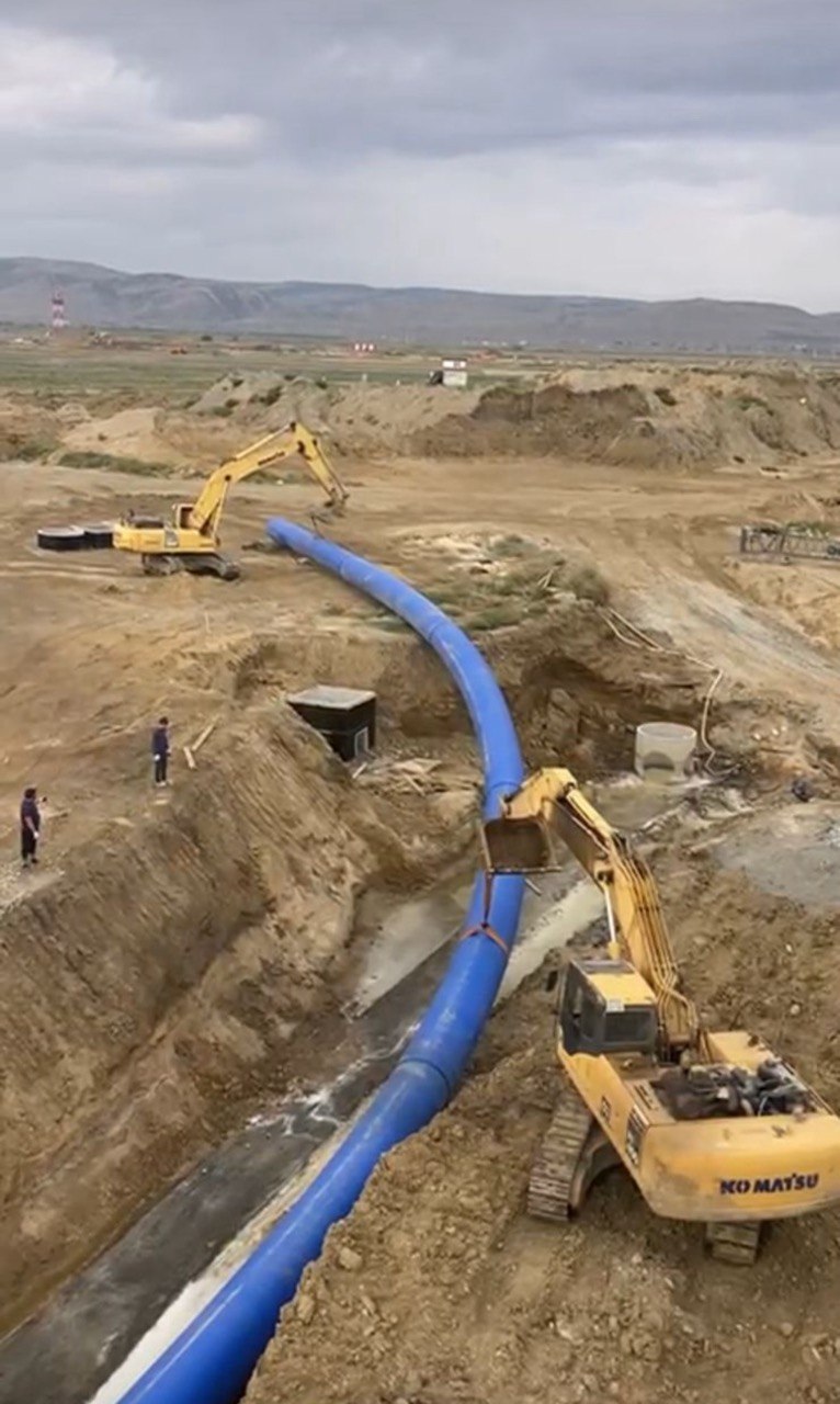 Два гусеничных экскаватора опускают плеть трубы в траншею